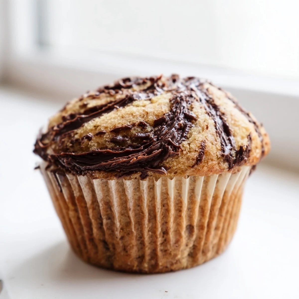 Freshly baked Nutella banana swirl muffins with golden tops and marble chocolate hazelnut ribbons