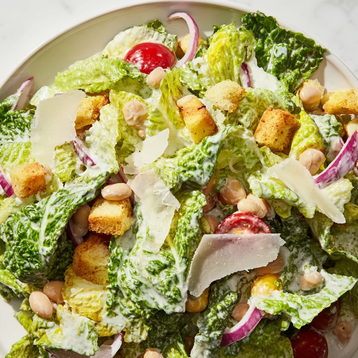 Creamy butter bean Caesar salad topped with shaved Parmesan and crunchy croutons on white plate