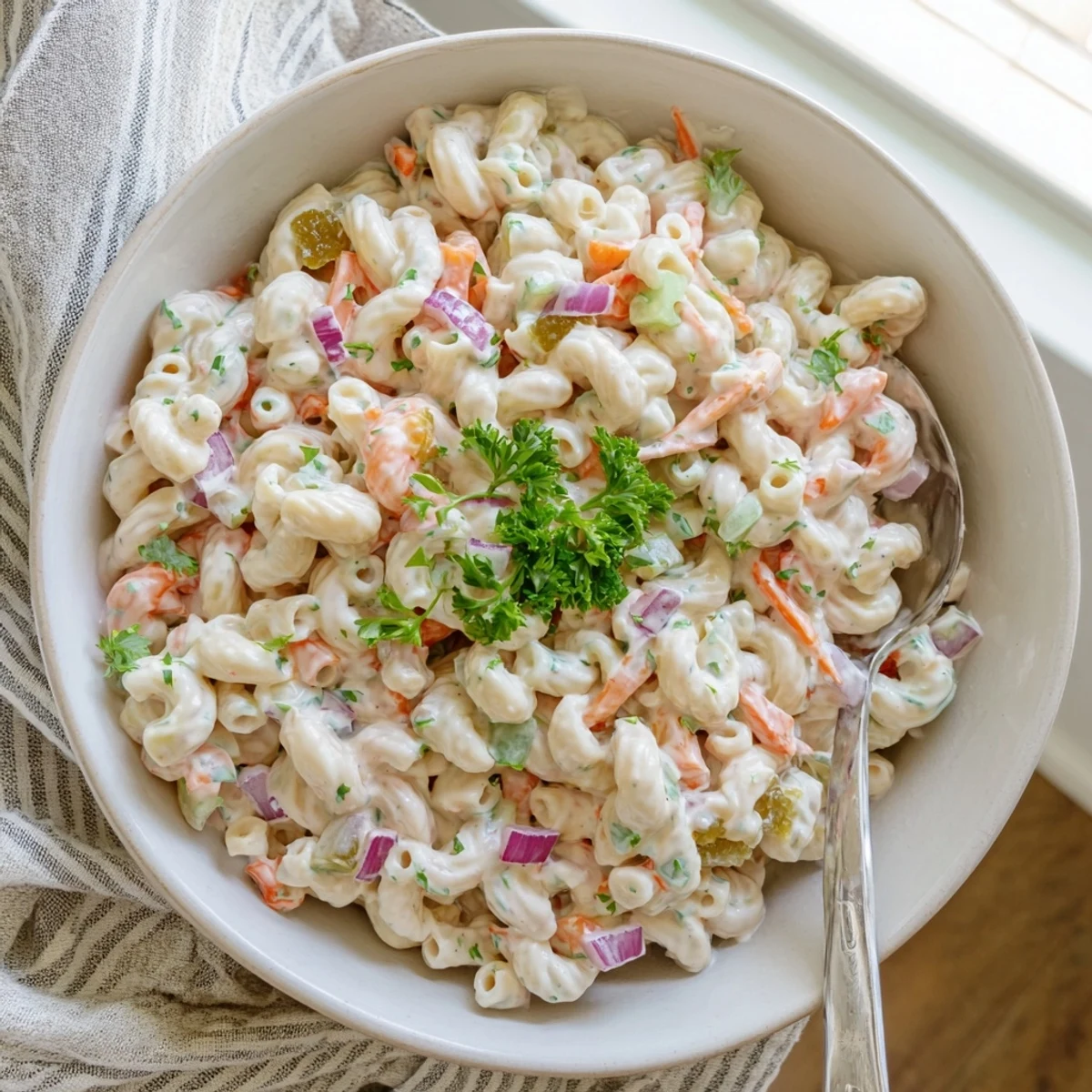 Creamy macaroni salad plated in a white serving dish featuring tender pasta elbows, diced red onion, and vibrant vegetables in a tangy mustard dressing