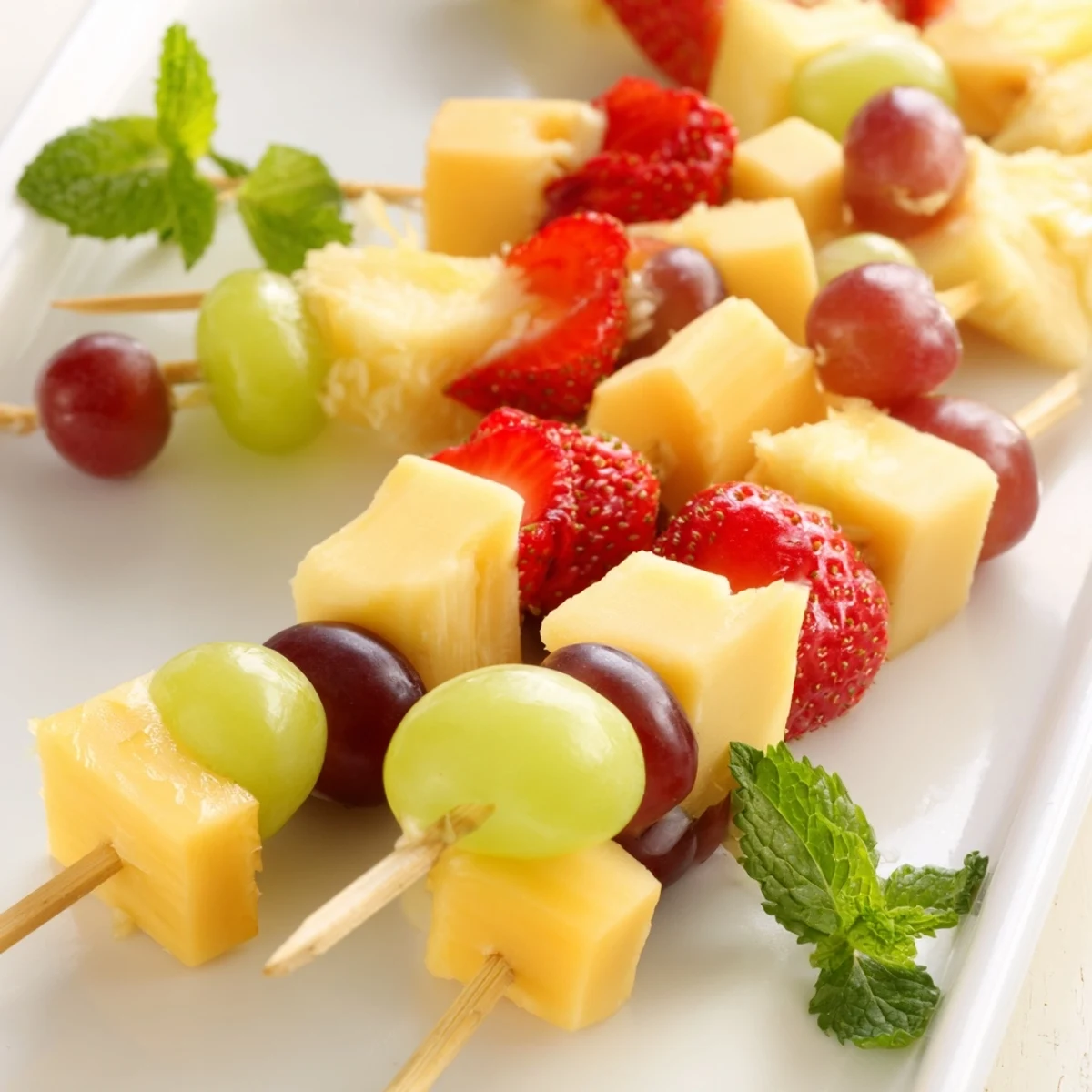 Colorful fruit and cheese kabobs featuring alternating red grapes, pineapple chunks, and creamy Monterey Jack cheese skewers.
