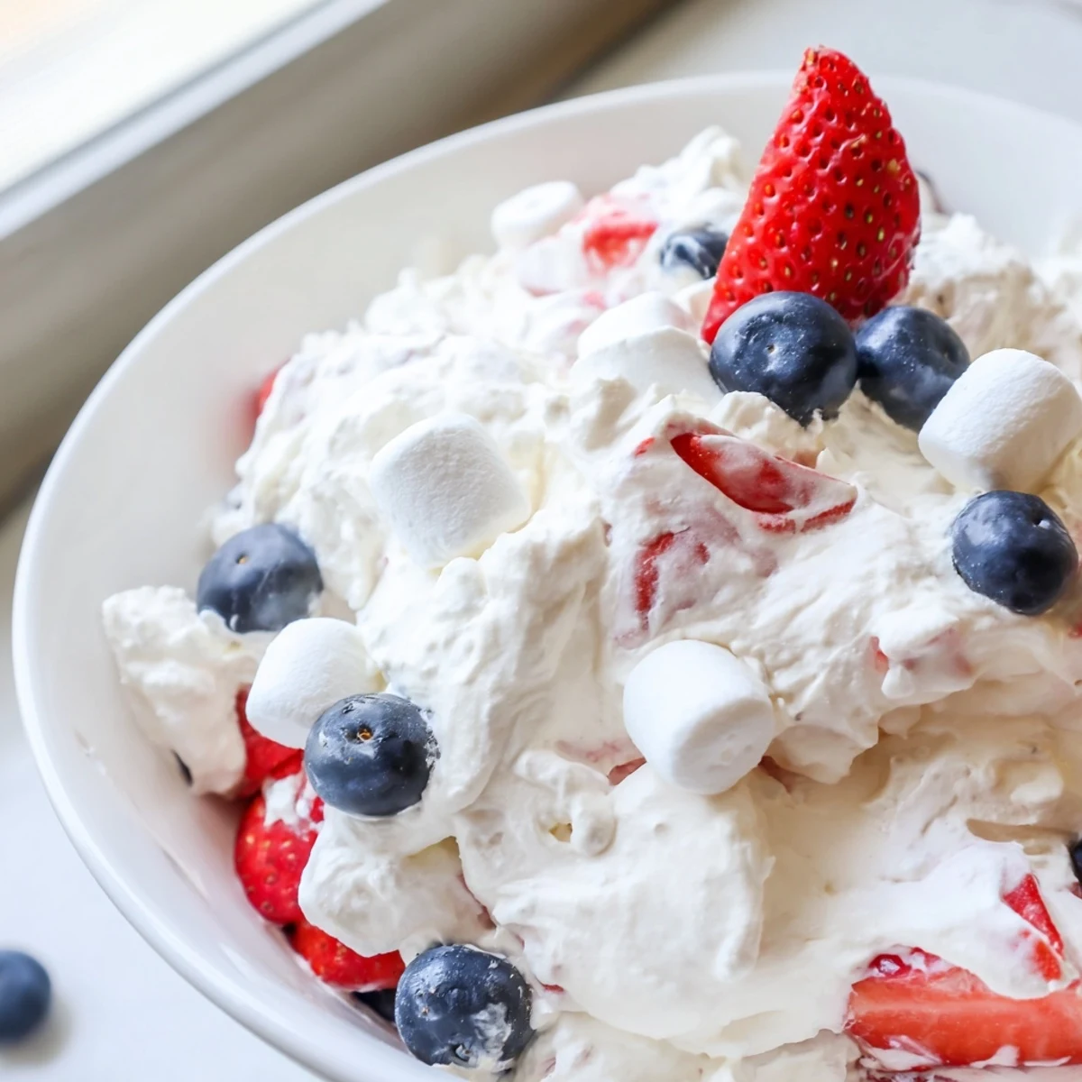 Red white blue cheesecake salad scooped into individual cups with plump juicy berries