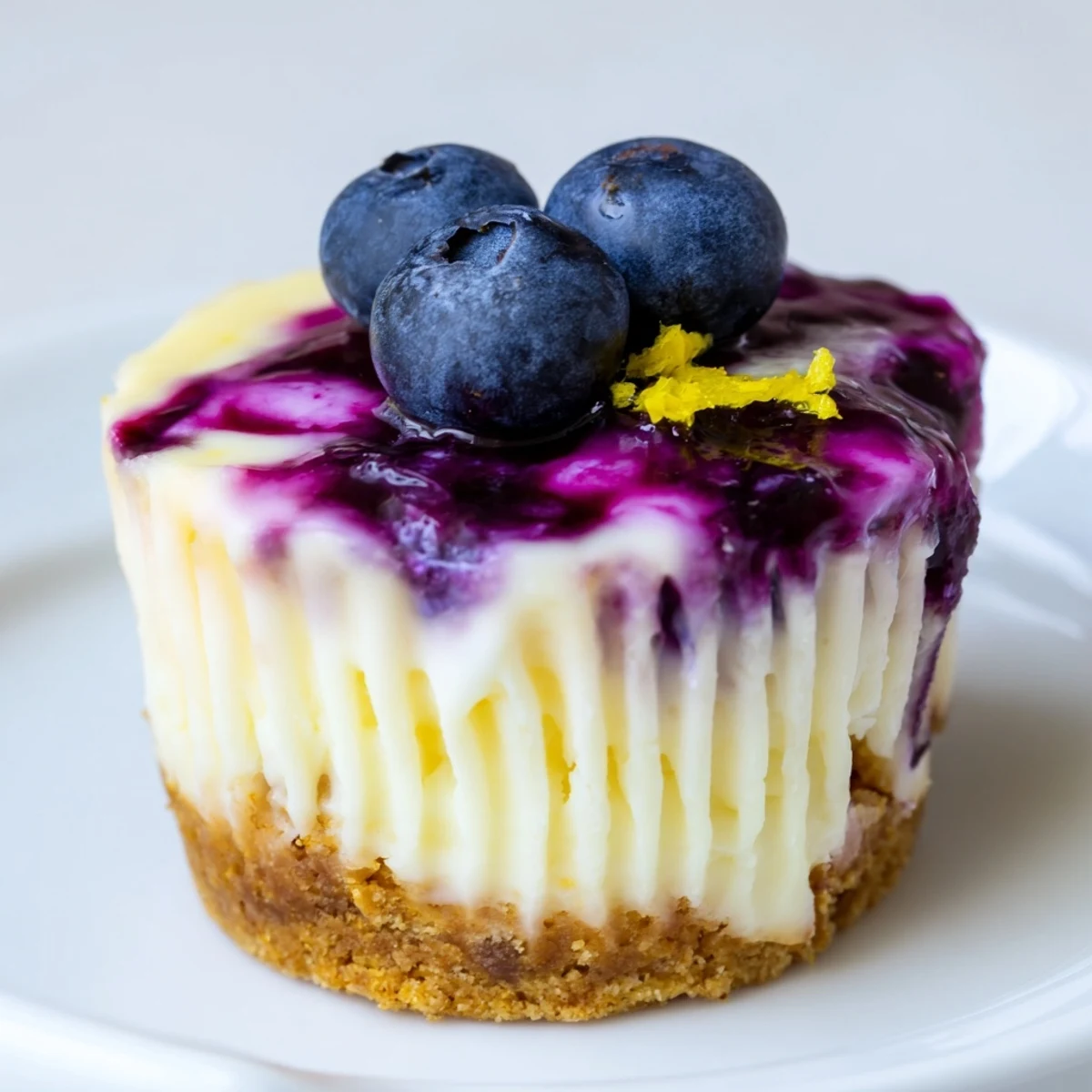 Creamy mini lemon blueberry cheesecakes with swirled topping in paper liners fresh from the oven