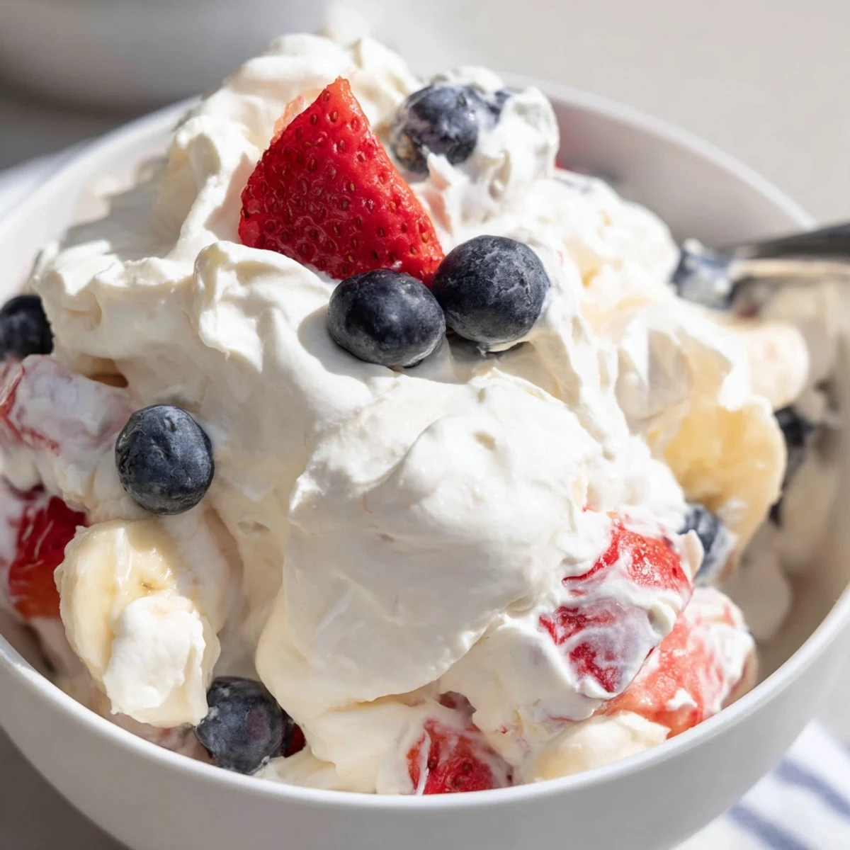 Spoon-ready Red White And Blue Cheesecake Salad, cool fluffy texture, berry garnish.