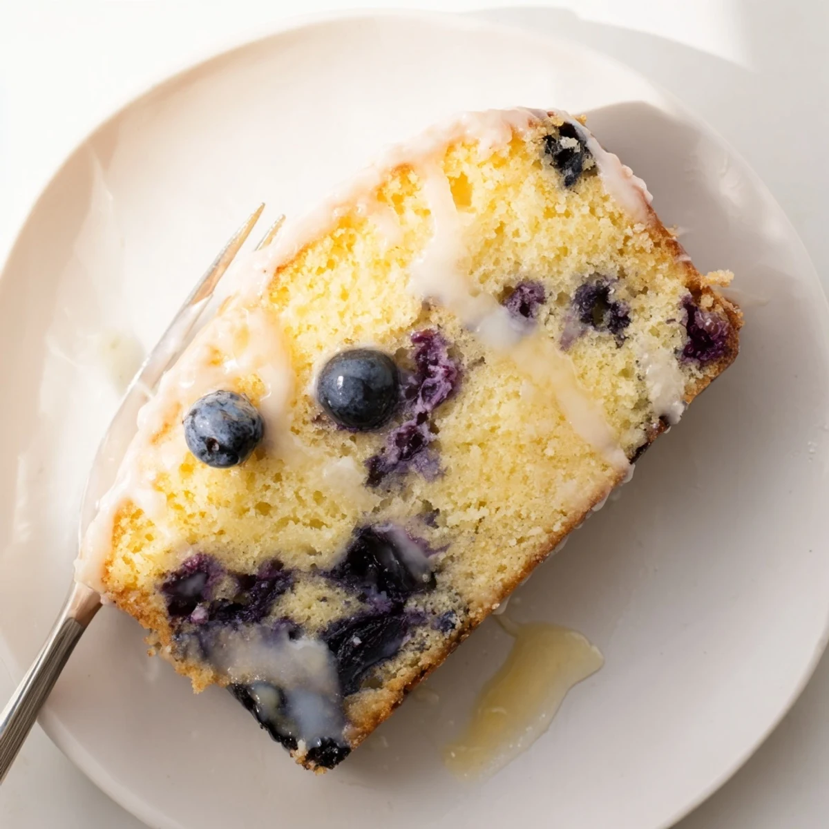 Moist lemon blueberry cake slice on a white plate with fresh berries and tea