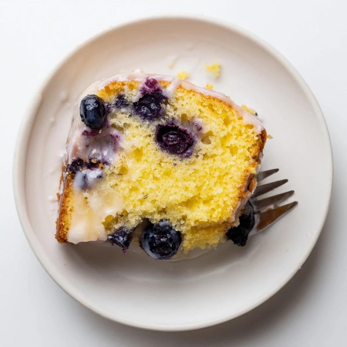 Golden lemon blueberry cake drizzled with white glaze and dotted with purple blueberries