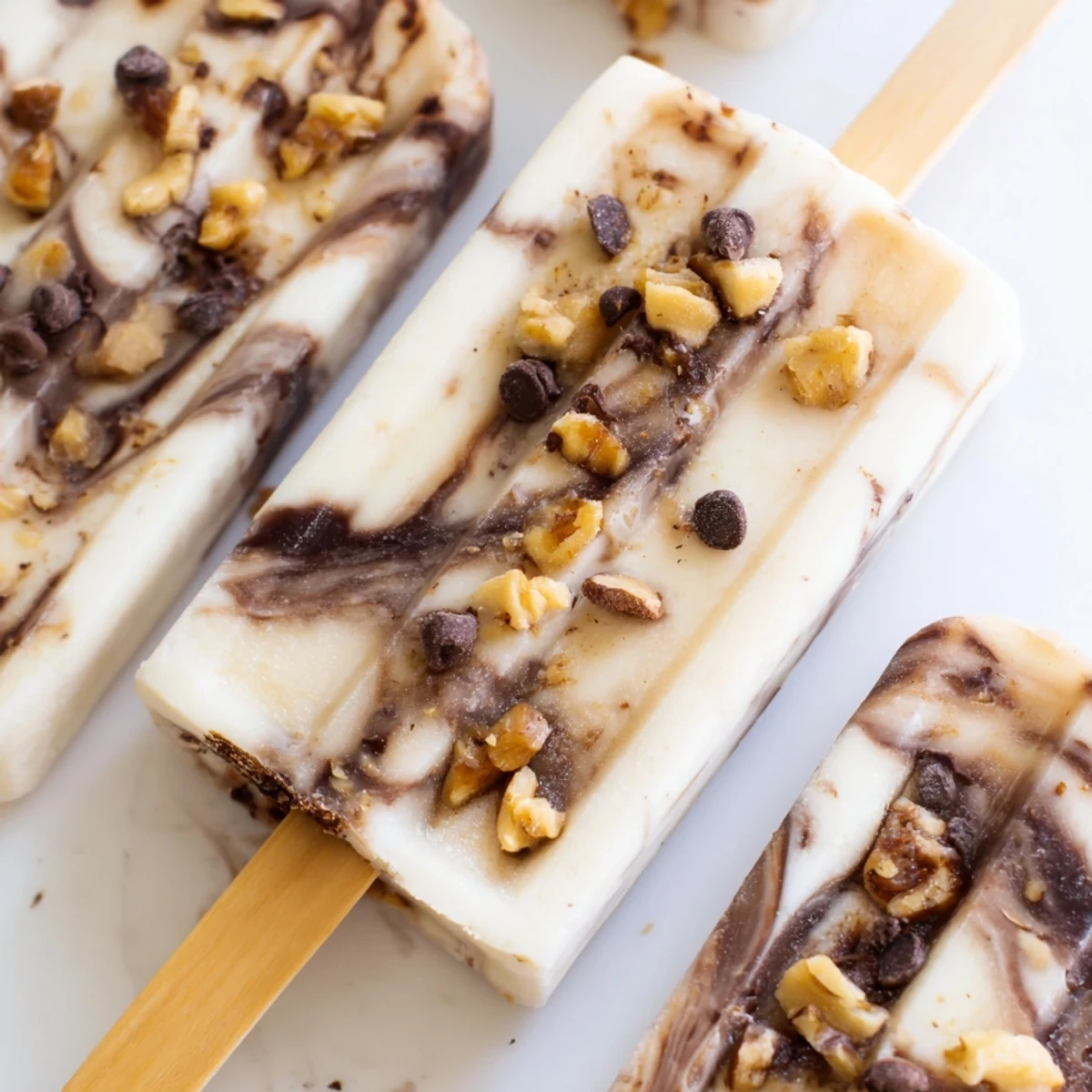 Frozen banana popsicles featuring rich chocolate marbling and creamy vanilla Greek yogurt base