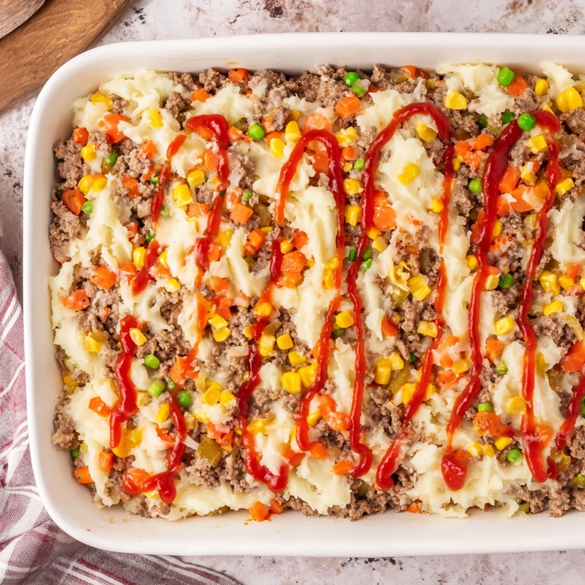 Savory meatloaf casserole with ketchup drizzle and cheesy mashed potato crust on a rustic wooden table
